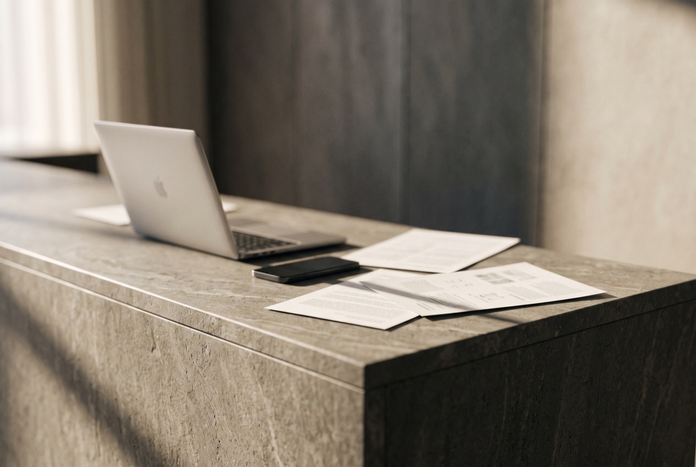 Mostrador de recepción con una notebook, un teléfono y papeles sueltos desalineados